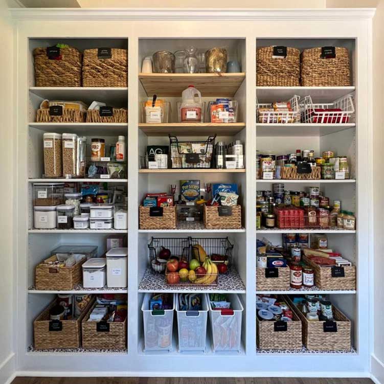 Decluttered then organized built-in pantry shelves with labeled organizing baskets, airtight acrylic containers with decanted pantry staples, and metal baskets with extra backstock items.