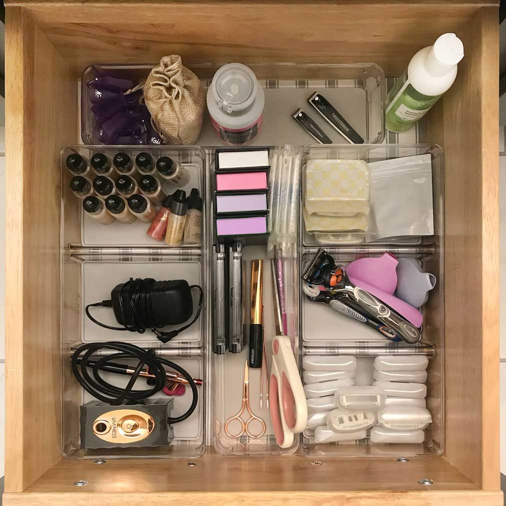 Organized vanity drawer with protective shelf liners and clear acrylic storage containers to declutter and store toiletries, makeup, and beauty tools.