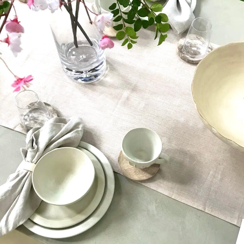 Staged and styled dining table with table runner, floral arrangement and designer tableware by Caitlin Ruth