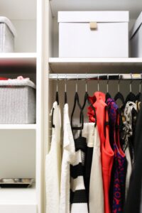 White built-in closet with adjustable shelves, black velvet hangers and organizing containers. The organizing containers are holding accessories, swimsuits and workout wear. Short dresses are hanging on the velvet hangers. In Roswell, GA